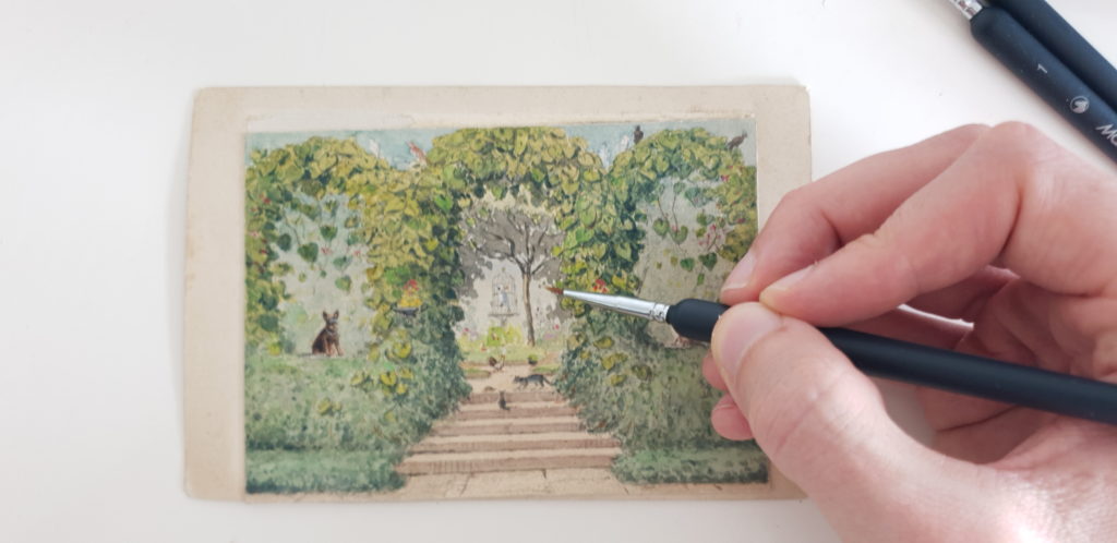 a man's hand painting a miniature watercolour painting with a fine detail brush